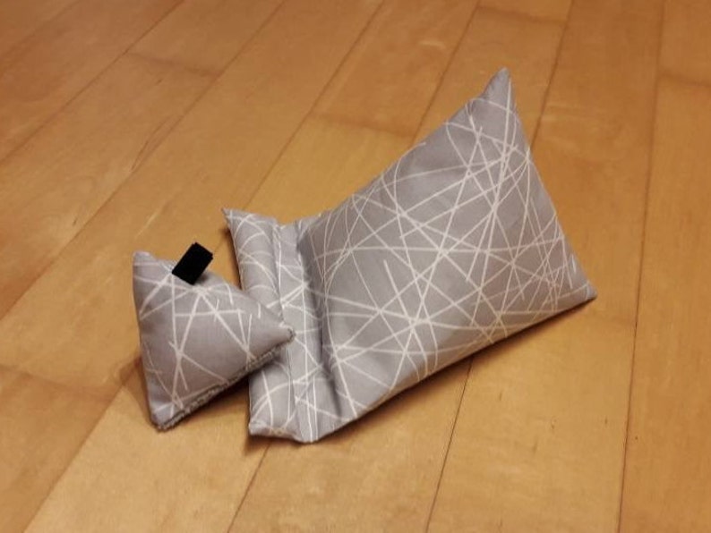 K&ouml;nnte beinhalten: Zwei graue Stoffkissen mit einem wei&szlig;en geometrischen Muster. Das kleinere Kissen ist dreieckig und das gr&ouml;&szlig;ere Kissen ist rechteckig.