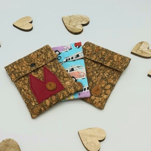 May include: Three small cork wallets with different fabric designs. One wallet has a red crown design, another has a blue and white design with vans, and the third has a pink and blue design with flowers.
