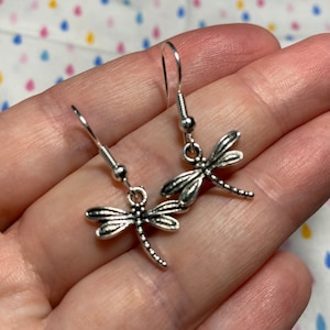 May include: A pair of silver dragonfly earrings with a delicate design. The earrings are on a white background.