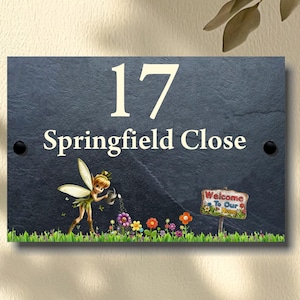 May include: Black slate house number sign with white lettering. The number 17 and the street name Springfield Close are displayed. A whimsical fairy with wings and a watering can is watering flowers. A sign reads "Welcome to Our Home".