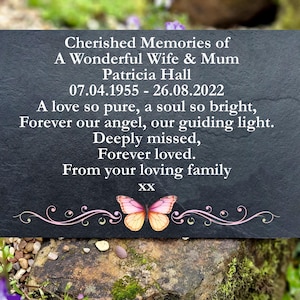 May include: A dark grey memorial plaque with white text, including the words "Cherished Memories" and a butterfly illustration. The plaque commemorates Patricia Hall, with dates 07.04.1955 - 26.08.2022, and is surrounded by flowers.