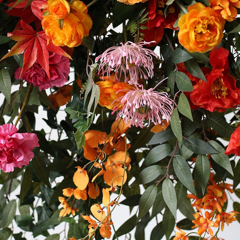 May include: A floral arrangement with a variety of flowers in shades of orange, pink, and red. The arrangement includes orange roses, pink proteas, and red poppies. The flowers are arranged in a lush, cascading style.