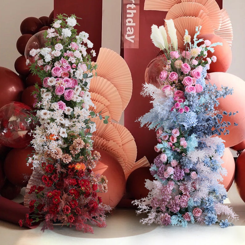 May include: Two floral arrangements with pink, white, and blue flowers, surrounded by peach and brown balloons. The text "birthday" is visible in the background.