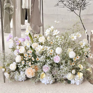 May include: A large arrangement of white, pink, and peach flowers with green foliage. The flowers are arranged in a vase on a white surface. The text "Transformation" and "Pure Rebirth" is visible in the background.