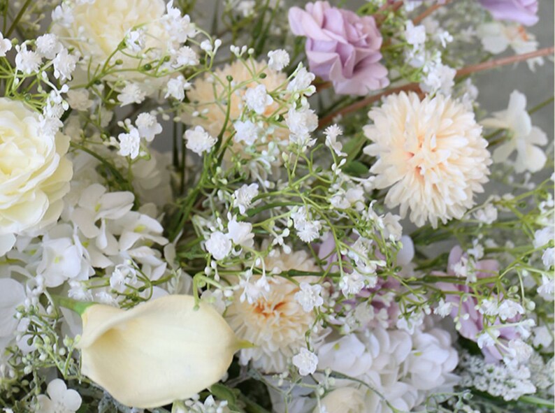 May include: A bouquet of white and cream flowers, including roses, carnations, and baby's breath. The flowers are arranged in a lush, romantic style.