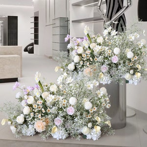 May include: Two large floral arrangements with white, pink, and lavender flowers in a modern setting. The flowers are arranged in a cascading style and are displayed on silver stands.