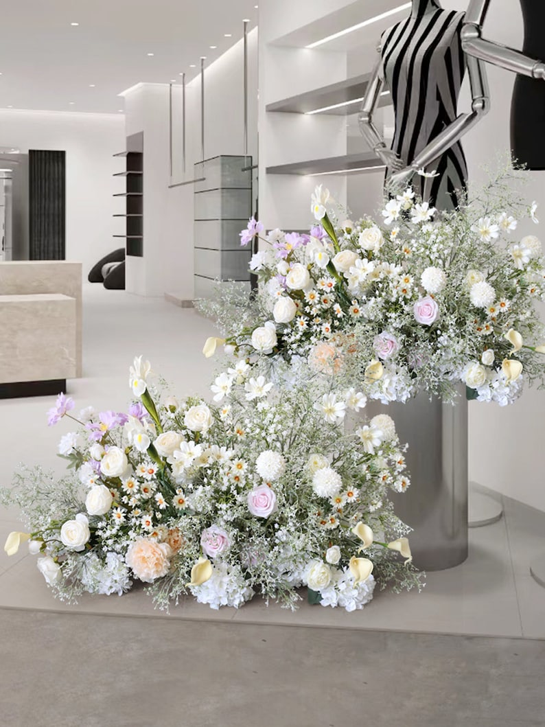 May include: Two large floral arrangements with white, pink, and lavender flowers in a modern setting. The flowers are arranged in a cascading style and are displayed on silver stands.