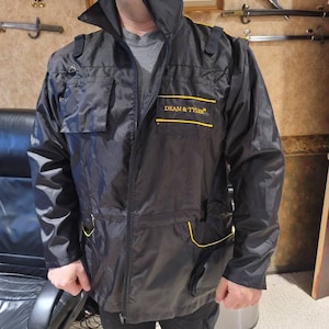 May include: A black jacket with yellow accents and the text "DEAN & TYLER" on the left chest. The jacket has a zipper closure and multiple pockets.