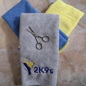 May include: Microfibre towels in blue, yellow, and grey, with small scissors on the grey towel. The grey towel has the embroidered text "2K9s" and a logo.