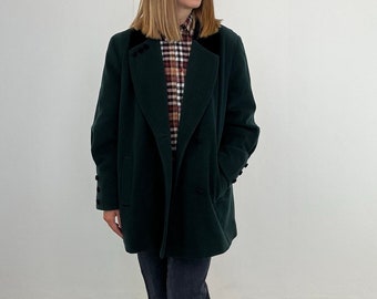Puede incluir: Un abrigo verde oscuro de doble botonadura con cuello de terciopelo negro. El abrigo se lleva sobre una camisa a cuadros.