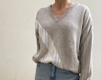 May include: A beige sweater with a white geometric pattern. The sweater has a v-neck and long sleeves. The person is wearing blue jeans with gold embellishments.