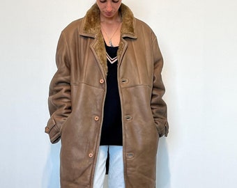 Könnte beinhalten: Eine braune Lederjacke mit einem Pelzkragen und einem schwarzen Shirt darunter. Die Person trägt eine weiße Hose und schwarze Stiefel.