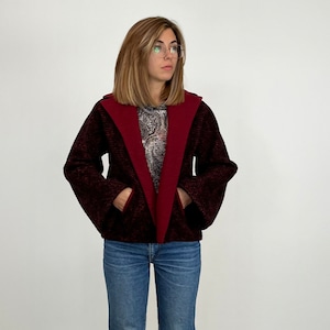 Puede incluir: Una chaqueta de capucha color burdeos con un diseño estampado en blanco y negro. La chaqueta tiene un corte holgado y está hecha de una tela suave y cómoda.