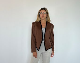 May include: A brown blazer with black trim and a single button closure. The blazer has a collarless design and a slightly cropped length. The model is wearing the blazer with a white top and light brown pants.