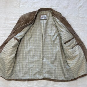 May include: A brown suede jacket with a plaid lining. The jacket has a button closure and two pockets on the inside.