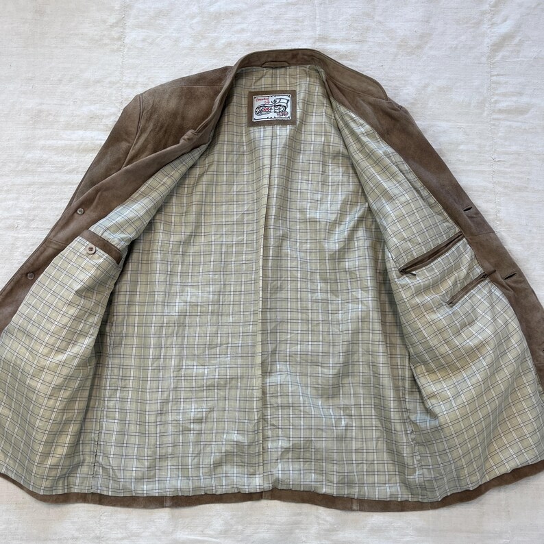 May include: A brown suede jacket with a plaid lining. The jacket has a button closure and two pockets on the inside.