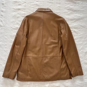 May include: A brown leather jacket with a button-up collar and a single-breasted closure. The jacket has a smooth, polished finish and a classic design.