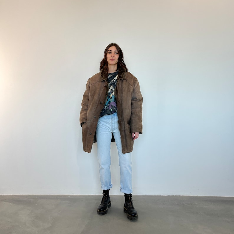 Puede incluir: Una chaqueta de ante marr&oacute;n con forro de piel de oveja. La chaqueta tiene cierre de botones y dos bolsillos. La persona que lleva la chaqueta tambi&eacute;n lleva pantalones vaqueros azules claros y botas negras.