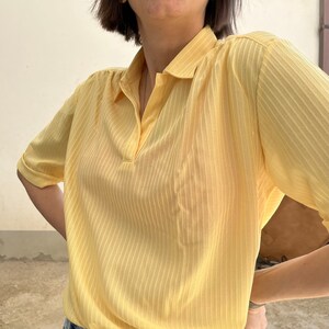 May include: A yellow short-sleeved collared shirt with vertical stripes. The shirt has a button-up closure and a pointed collar.