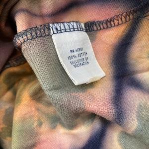 May include: A white tag sewn into a garment with the text "RN 41381 100% COTTON EXCLUSIVE OF DECORATION".