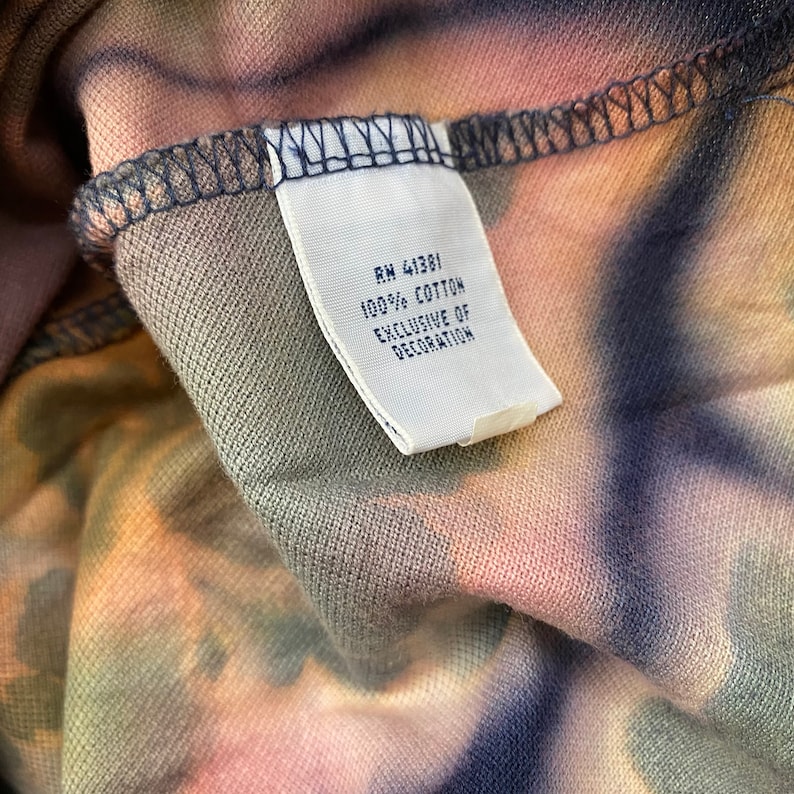 May include: A white tag sewn into a garment with the text "RN 41381 100% COTTON EXCLUSIVE OF DECORATION".