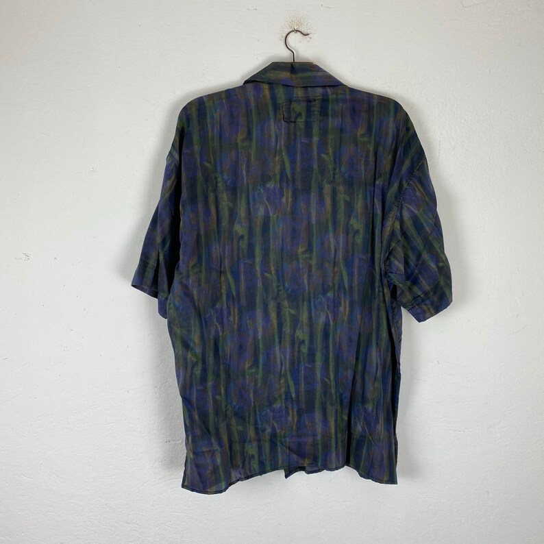 May include: A short-sleeved button-up shirt with a dark blue, green, and purple abstract print.