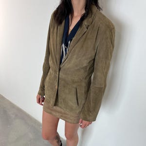 May include: A brown suede blazer with a single button closure and a long sleeve. The blazer is worn over a striped shirt.