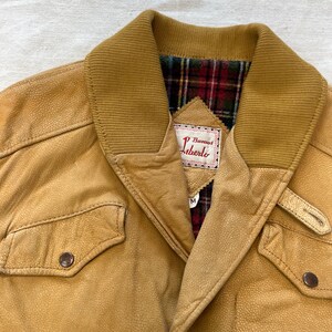 May include: A tan leather jacket with a plaid lining and a label that reads "D'Bueno's Liberto".