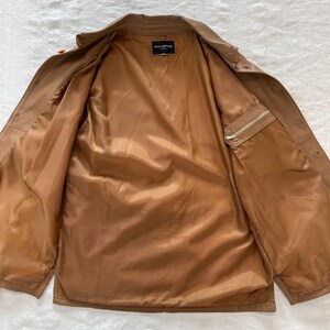 May include: A brown leather jacket with a zippered pocket on the left sleeve and a label that reads "Gianfranco Ferre" on the inside collar.