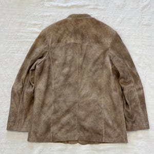 May include: A brown suede jacket with a stand-up collar and a button closure. The jacket has a distressed look and is made of soft, supple leather.