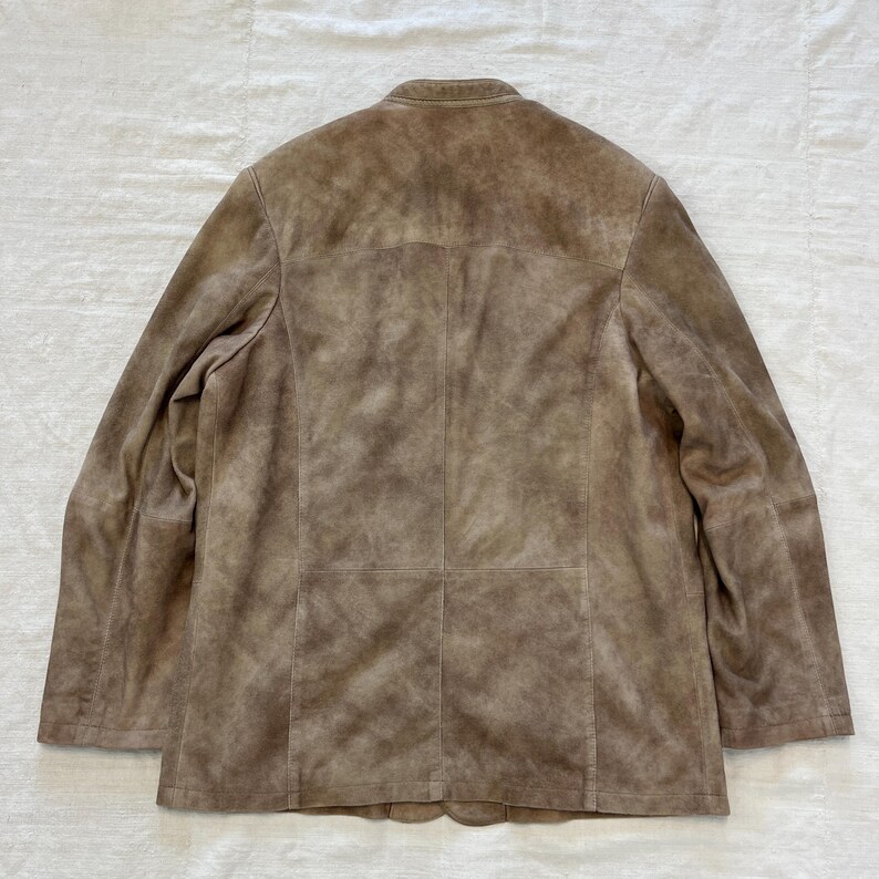 May include: A brown suede jacket with a stand-up collar and a button closure. The jacket has a distressed look and is made of soft, supple leather.