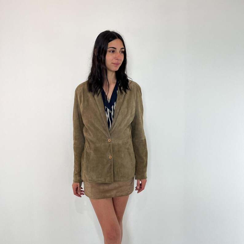 May include: A brown suede blazer with a single button closure. The blazer has long sleeves and a collar.