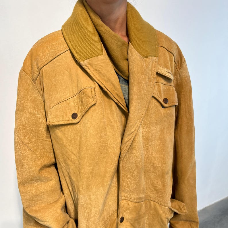 May include: A tan leather jacket with a brown corduroy collar. The jacket has a zipper closure and two flap pockets on the front.