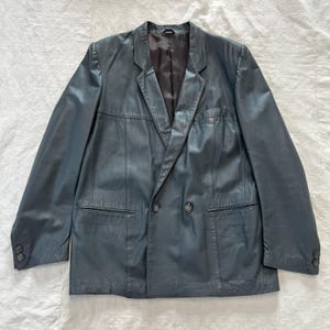 Op de afbeelding: Een donkerblauwe leren blazer met een dubbele rij knopen en twee zakken aan de voorkant.