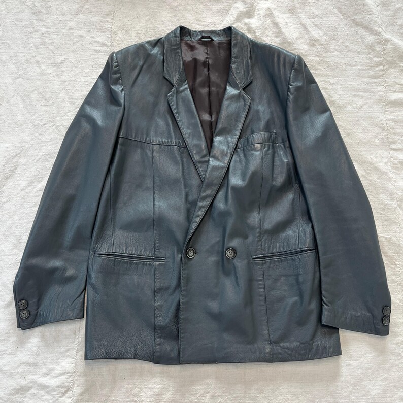 Op de afbeelding: Een donkerblauwe leren blazer met een dubbele rij knopen en twee zakken aan de voorkant.