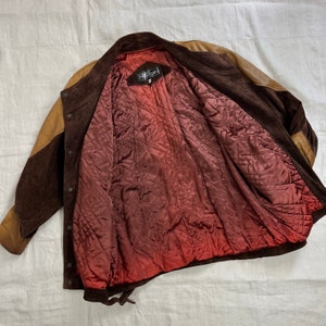 May include: Brown suede jacket with a tan suede panel on the left side. The jacket has a red quilted lining and a black label that says "FREECOURT".