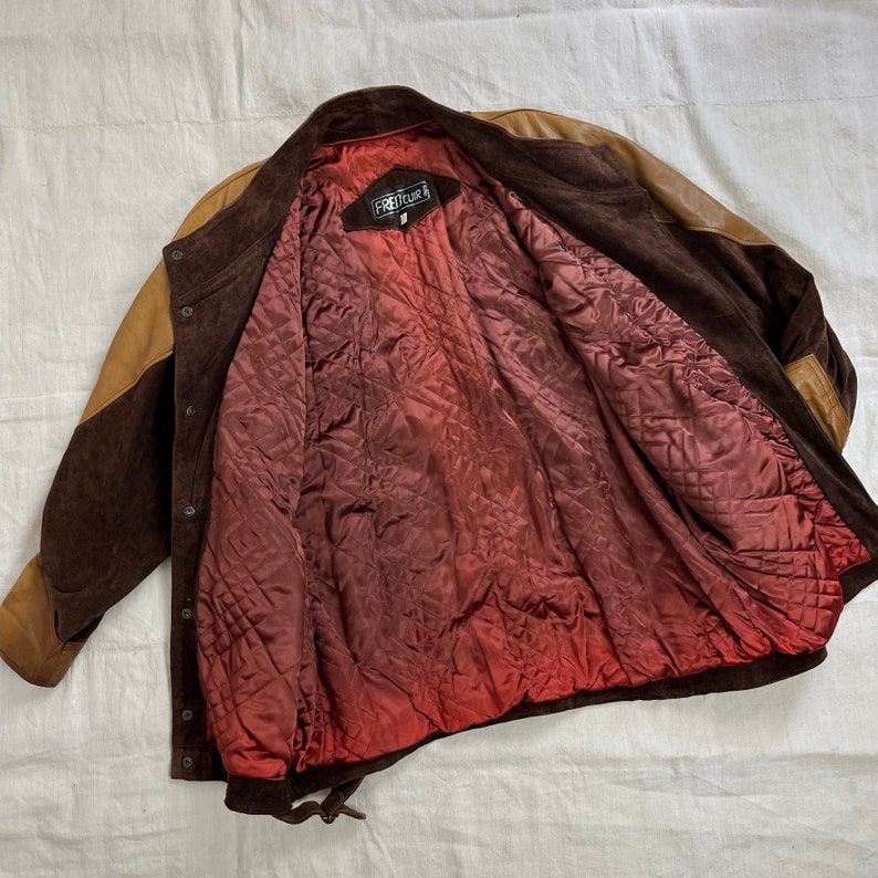 May include: Brown suede jacket with a tan suede panel on the left side. The jacket has a red quilted lining and a black label that says "FREECOURT".