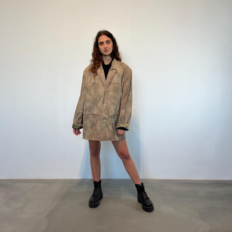 May include: A brown suede jacket with a button-up front and a relaxed fit. The jacket has a tie-dye pattern and is worn by a person with long brown hair.