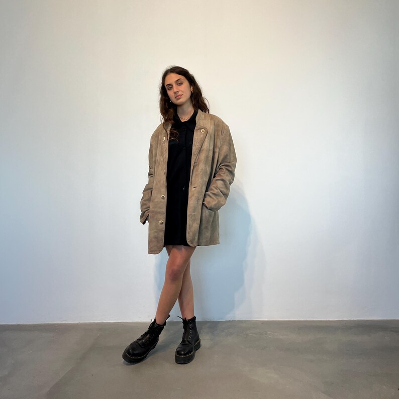 May include: A person wearing a brown suede jacket with a black shirt and black boots.