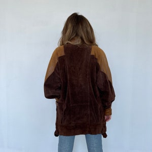 May include: A brown suede jacket with brown leather sleeves. The jacket has a zipper closure and a stand-up collar.