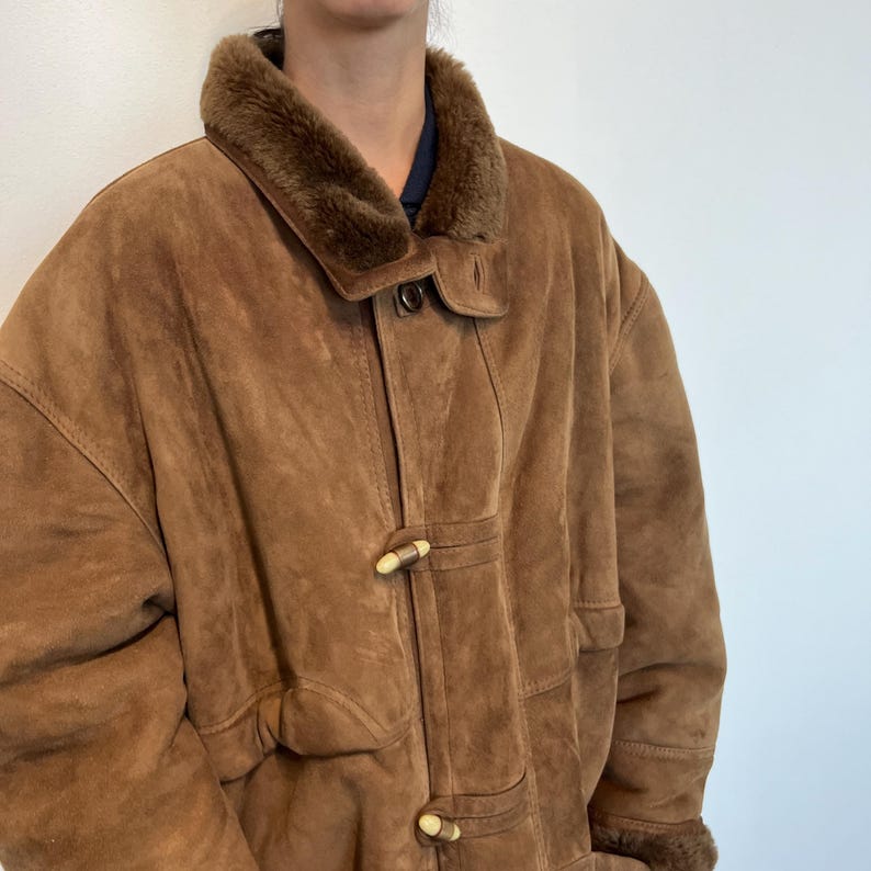 May include: A brown suede jacket with a faux fur collar and toggle closures. The jacket has a relaxed fit and is lined with a soft, warm material.