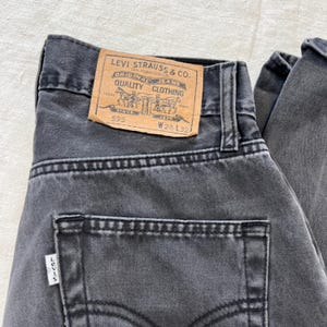 May include: Close-up of a pair of faded black Levi's jeans. The back pocket and the Levi's label are visible. The label reads "LEVI STRAUSS & CO. ORIGINAL JEANS QUALITY CLOTHING" with the numbers "595", "W28 L32", and the Levi's logo.