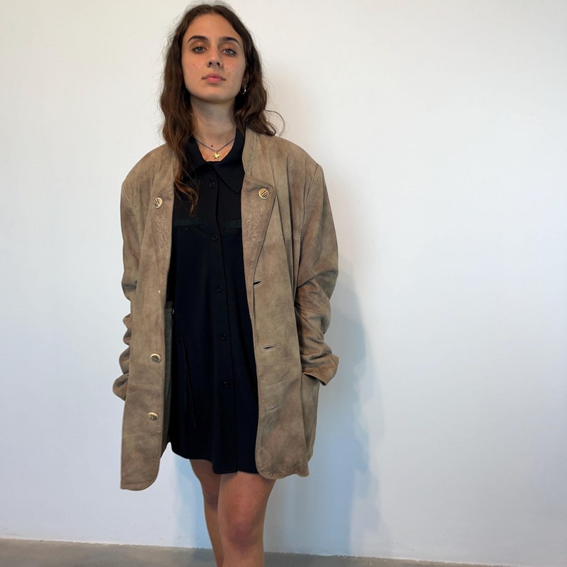 May include: A brown suede jacket with a button closure and a black shirt underneath.