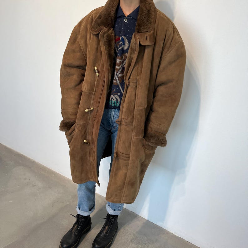 May include: A brown sheepskin coat with a fur collar and a button closure. The coat is long and has a relaxed fit.
