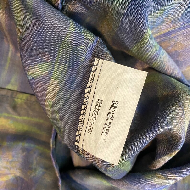 May include: A white tag with black text on a dark blue and green fabric. The tag reads "VISCOSA-VISCOSE 100% VISCOSE-VISKOSE norma della legge 883 del 26-11-1973".
