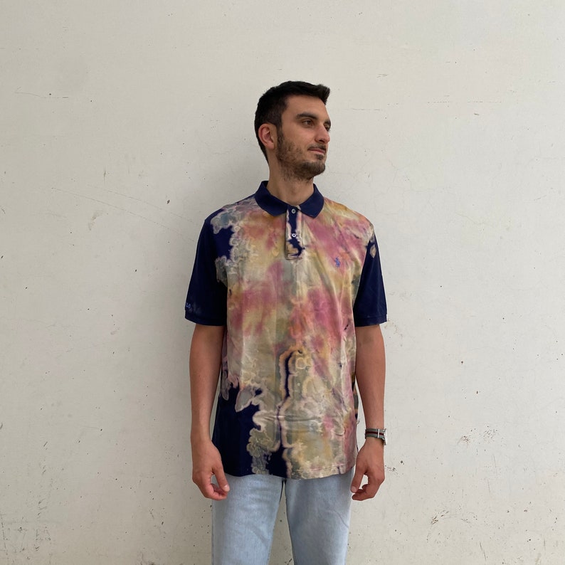 May include: A navy blue polo shirt with a tie-dye pattern in shades of pink, yellow, and green. The shirt has a button-up collar and short sleeves.