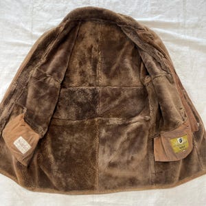 May include: Brown sheepskin shearling jacket with a zipper closure and two pockets. The jacket is lined with brown fur and has a brown leather collar.
