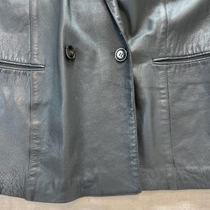 Op de afbeelding: Een zwart leren blazer met een dubbele knoopsluiting en twee knoopaccenten.