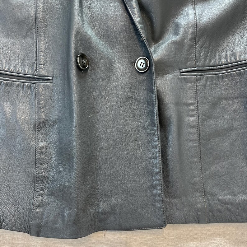 Op de afbeelding: Een zwart leren blazer met een dubbele knoopsluiting en twee knoopaccenten.