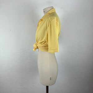 May include: A yellow short-sleeved collared shirt with a ribbed texture. The shirt is tied at the waist.